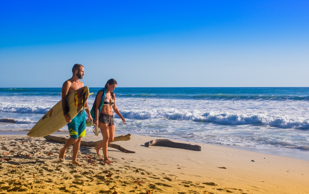 Santa Teresa, Costa Rica - surfers walking on the beachJune, 28, 2018: Couple of surfers on the beach of Santa Teresa walking and enjoying the time together in a beautiful sunny day with blue sky and blue water